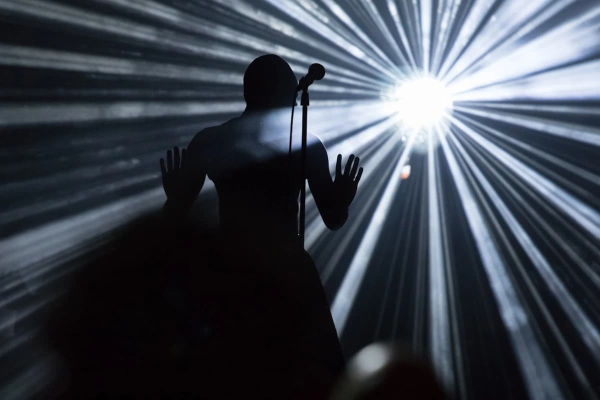 A singer silhouetted at a microphone in front of stage light beams